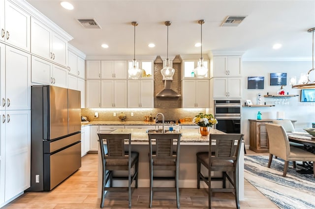 kitchen with pendant lighting, a center island with sink, light stone countertops, and appliances with stainless steel finishes