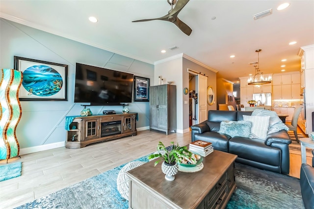 living room featuring ornamental molding, a barn door, ceiling fan with notable chandelier, and light hardwood / wood-style floors