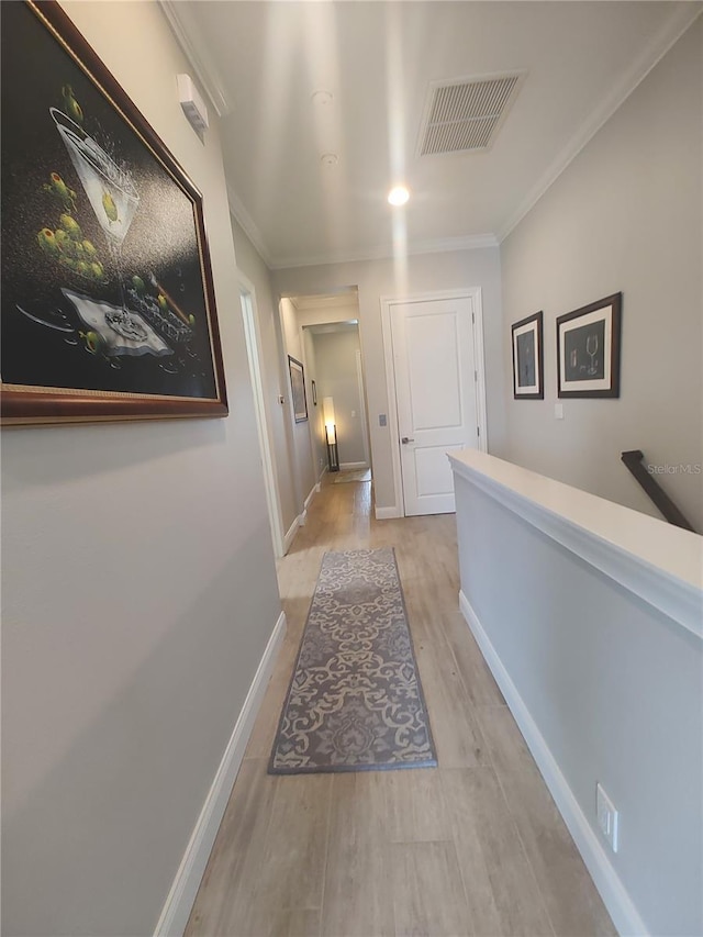 corridor with light wood finished floors, ornamental molding, baseboards, and visible vents