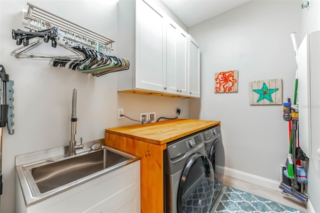 clothes washing area featuring a sink, cabinet space, independent washer and dryer, wood finished floors, and baseboards