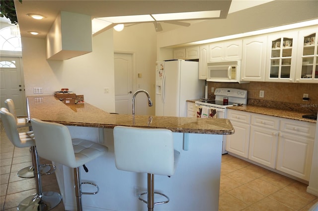 kitchen featuring sink, white cabinets, a kitchen breakfast bar, light stone counters, and white appliances