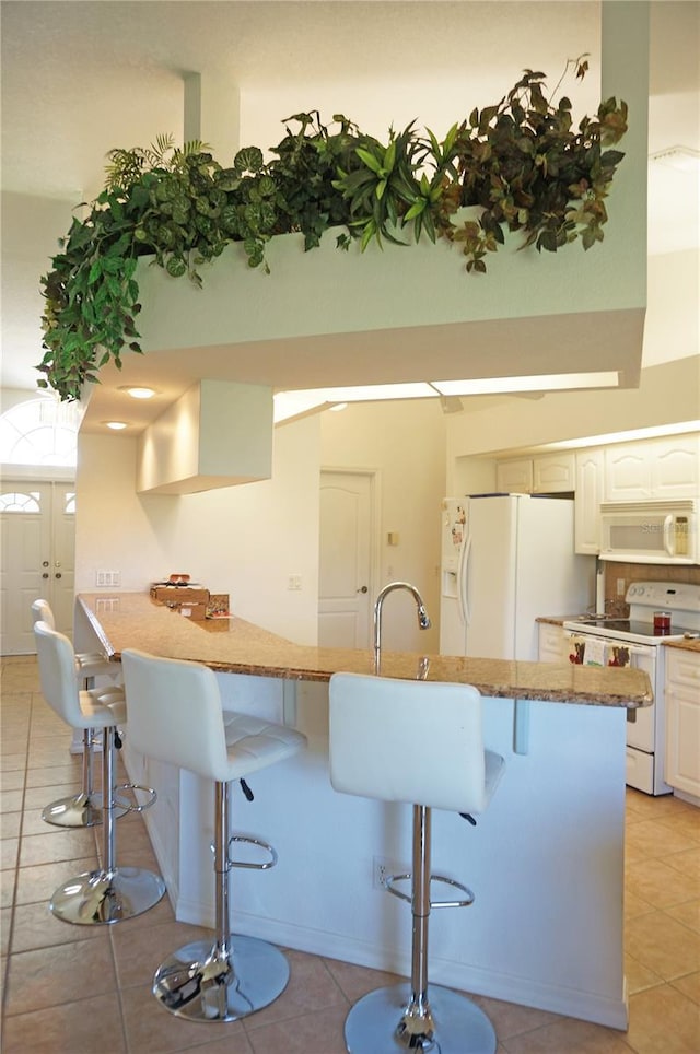 kitchen featuring white cabinetry, white appliances, a kitchen breakfast bar, and light tile patterned flooring