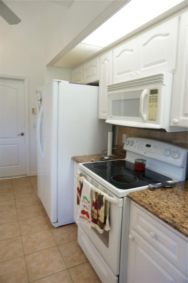 kitchen with white cabinetry, light tile patterned floors, white appliances, and dark stone counters