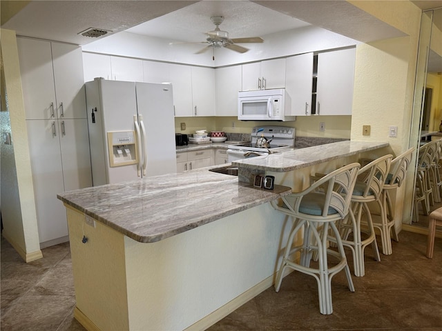 kitchen with white appliances, a kitchen breakfast bar, kitchen peninsula, and white cabinets