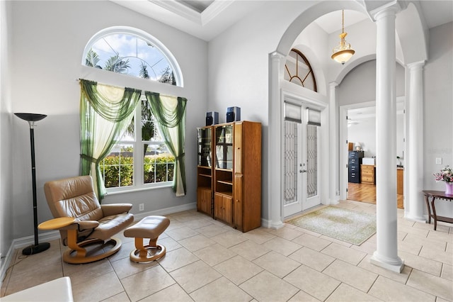 living area featuring a towering ceiling, light tile patterned floors, and decorative columns