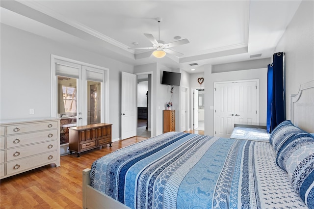 bedroom featuring ceiling fan, connected bathroom, wood finished floors, french doors, and a raised ceiling