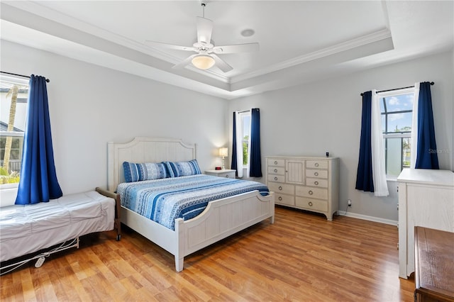 bedroom featuring ceiling fan, baseboards, light wood-style floors, a tray ceiling, and crown molding