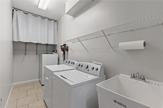 laundry room with laundry area, light tile patterned floors, baseboards, washing machine and dryer, and a sink