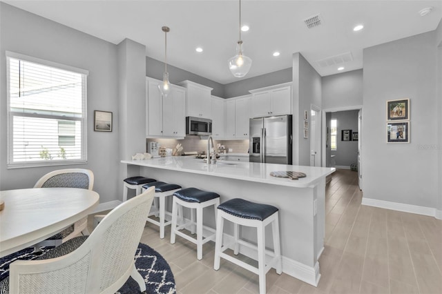 kitchen with appliances with stainless steel finishes, sink, white cabinets, backsplash, and hanging light fixtures