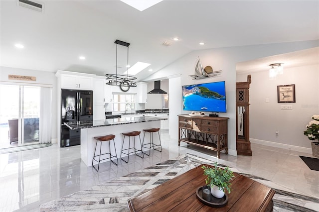 kitchen featuring wall chimney exhaust hood, sink, black fridge, a center island, and white cabinets