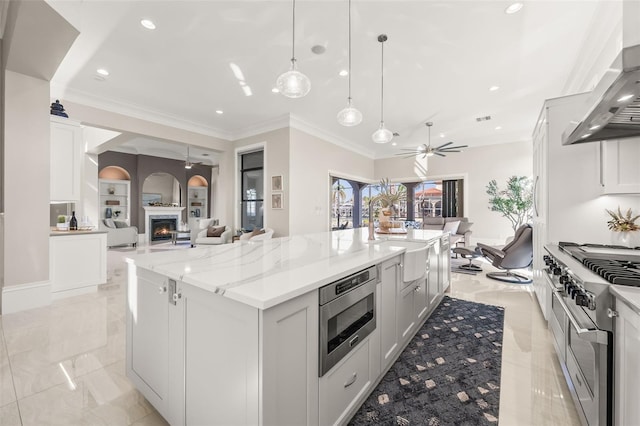 kitchen featuring decorative light fixtures, a large island, light stone counters, stainless steel appliances, and wall chimney range hood