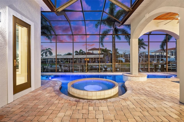 pool at dusk featuring a patio area, an in ground hot tub, and glass enclosure