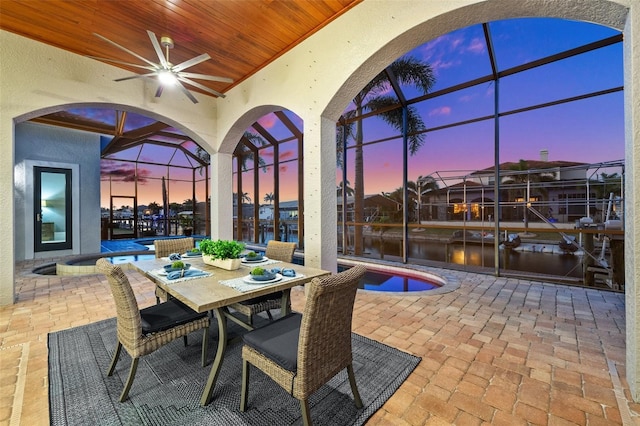 patio terrace at dusk featuring a water view, ceiling fan, and a lanai