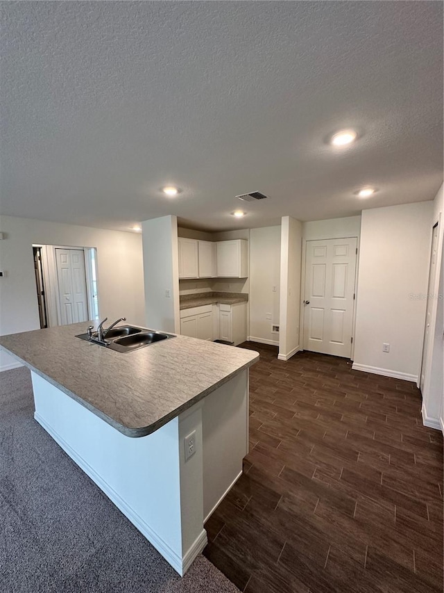 kitchen featuring visible vents, an island with sink, wood tiled floor, white cabinetry, and a sink