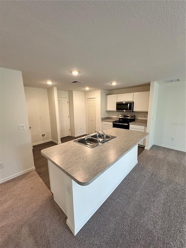 kitchen with stainless steel microwave, electric range, white cabinetry, a sink, and an island with sink