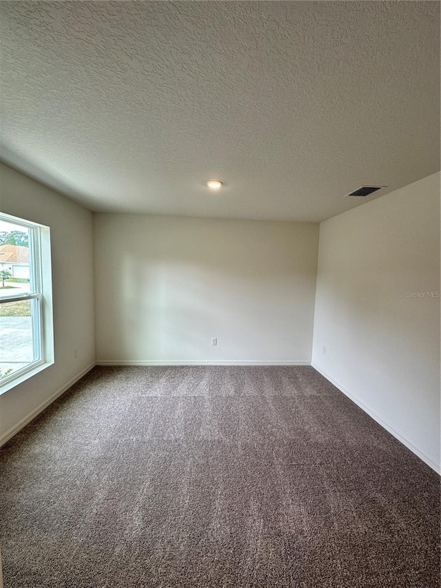 spare room with carpet floors, baseboards, visible vents, and a textured ceiling