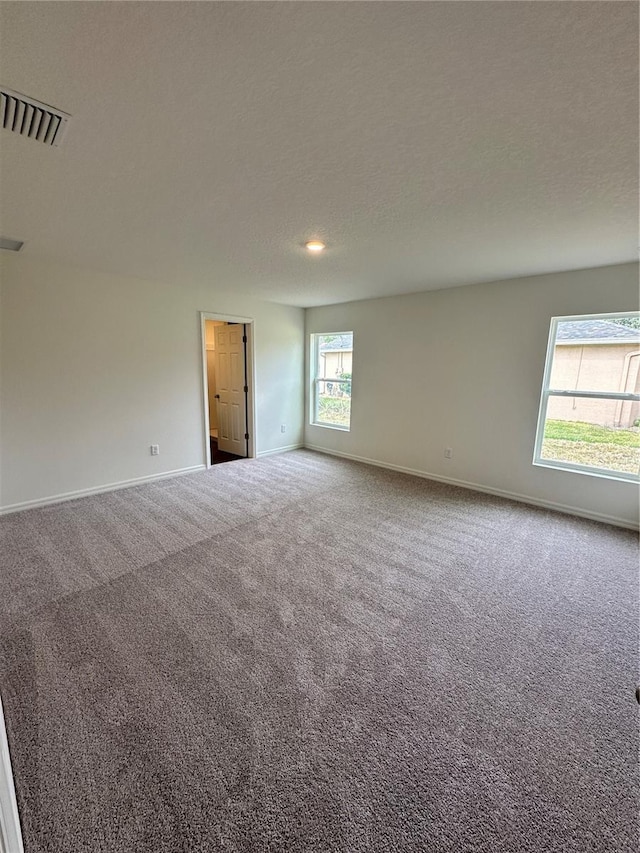 unfurnished room featuring carpet floors, baseboards, visible vents, and a textured ceiling