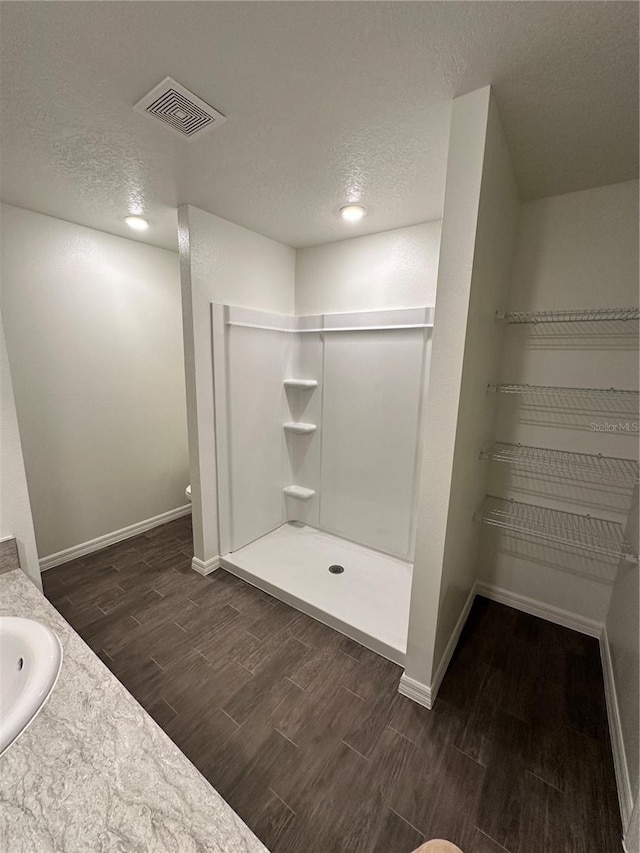 full bathroom featuring a textured ceiling, wood finish floors, visible vents, and baseboards