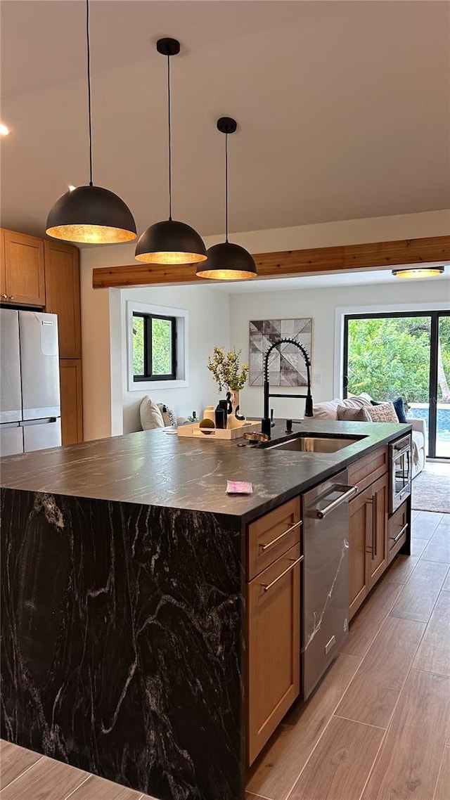 kitchen featuring sink, appliances with stainless steel finishes, a kitchen island with sink, decorative light fixtures, and light wood-type flooring