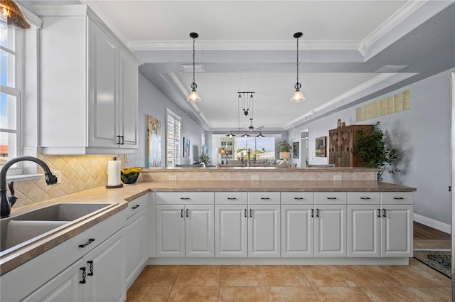 kitchen featuring sink, decorative light fixtures, ornamental molding, kitchen peninsula, and white cabinets