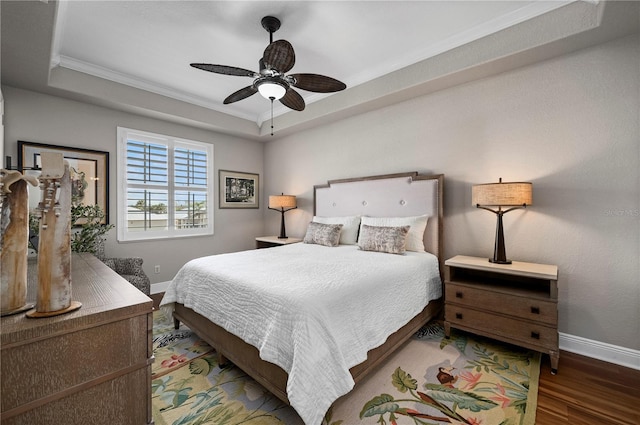 bedroom with dark hardwood / wood-style floors, ceiling fan, a tray ceiling, and crown molding