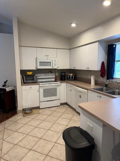 kitchen with white appliances, white cabinets, lofted ceiling, light countertops, and a sink