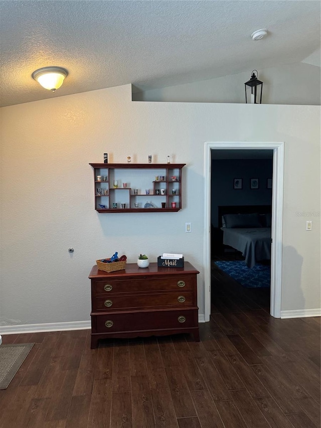 corridor with dark wood-type flooring, lofted ceiling, a textured ceiling, and baseboards