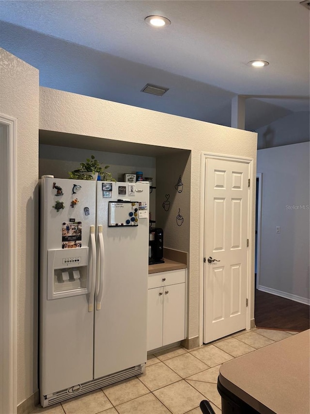 kitchen with light tile patterned floors, white refrigerator with ice dispenser, recessed lighting, and white cabinets