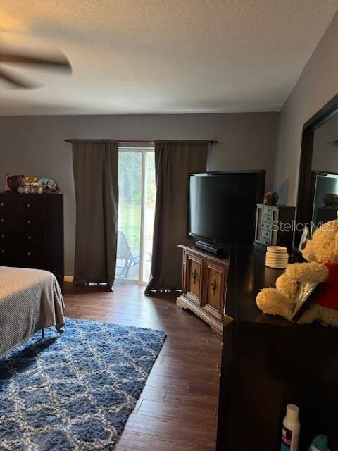 bedroom with a textured ceiling, dark wood finished floors, a ceiling fan, and access to exterior