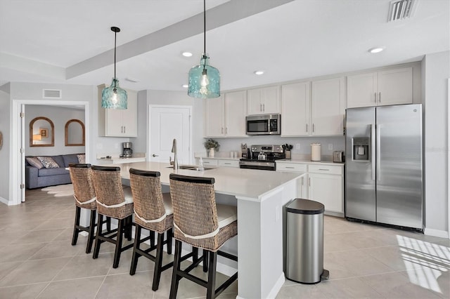 kitchen featuring appliances with stainless steel finishes, a center island with sink, light countertops, decorative light fixtures, and white cabinetry