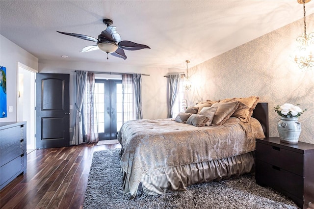 bedroom with ceiling fan with notable chandelier, access to outside, dark wood-type flooring, a textured ceiling, and french doors