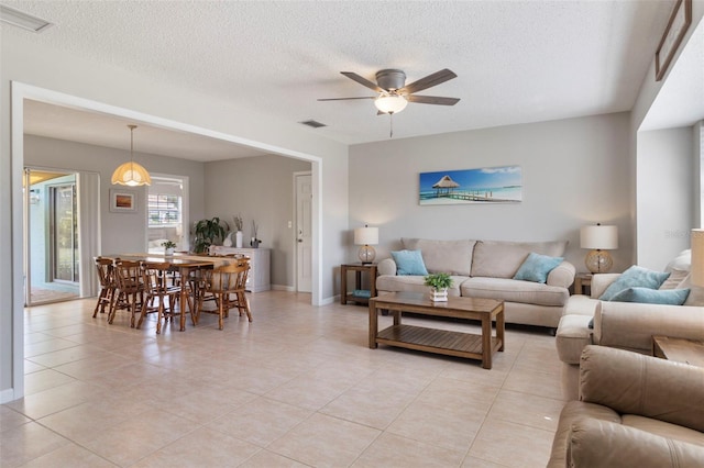 living area with a ceiling fan, visible vents, a textured ceiling, and light tile patterned floors