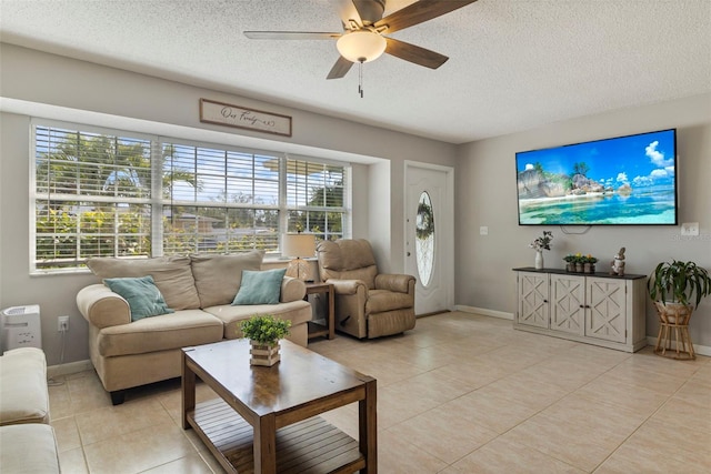 living area with light tile patterned floors, ceiling fan, baseboards, and a textured ceiling