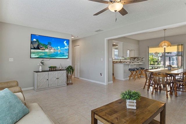 living area featuring baseboards, visible vents, ceiling fan, a textured ceiling, and light tile patterned flooring