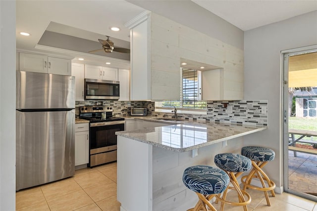 kitchen with light stone counters, appliances with stainless steel finishes, white cabinets, a sink, and a peninsula