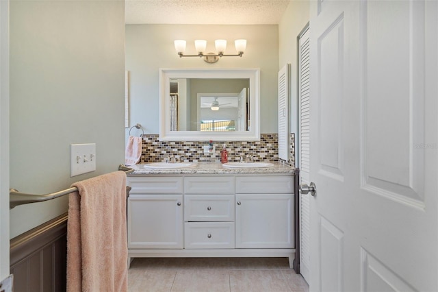 full bath featuring double vanity, a textured ceiling, decorative backsplash, and a sink