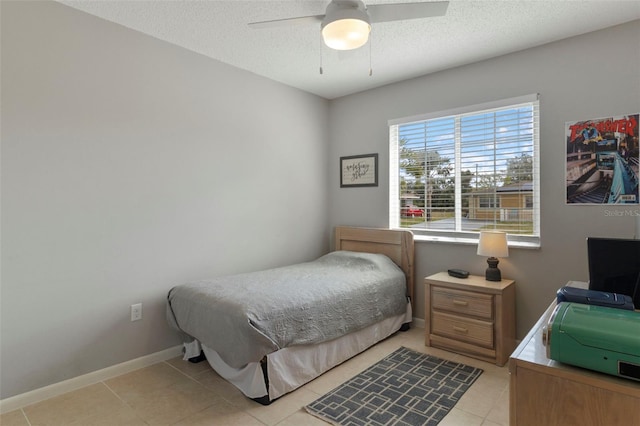 bedroom with ceiling fan, baseboards, a textured ceiling, and light tile patterned flooring