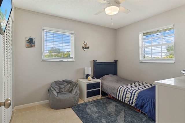 bedroom featuring ceiling fan, a textured ceiling, baseboards, and light tile patterned floors