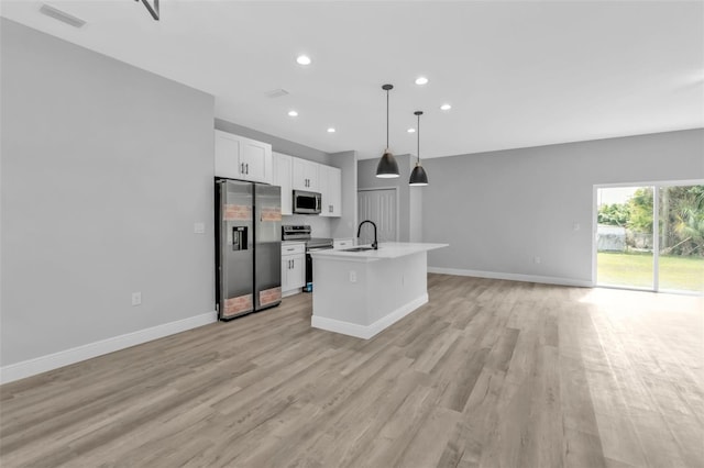 kitchen with sink, white cabinetry, hanging light fixtures, stainless steel appliances, and a center island with sink