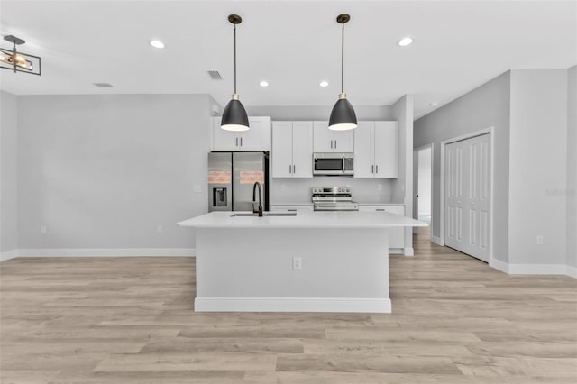 kitchen featuring sink, white cabinetry, stainless steel appliances, a center island with sink, and decorative light fixtures