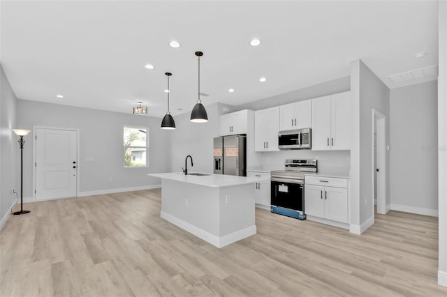 kitchen with appliances with stainless steel finishes, white cabinetry, sink, hanging light fixtures, and a center island with sink