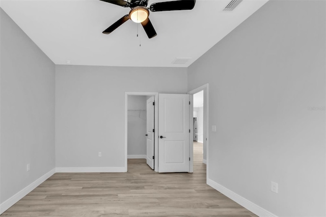 unfurnished bedroom featuring ceiling fan, a spacious closet, light wood-type flooring, and a closet