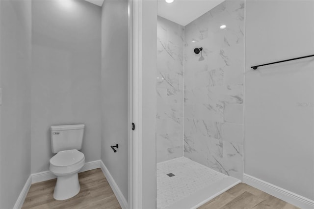 bathroom with hardwood / wood-style flooring, a tile shower, and toilet