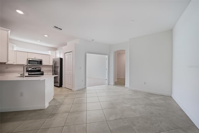 kitchen with sink, appliances with stainless steel finishes, white cabinetry, light tile patterned flooring, and kitchen peninsula