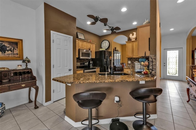 kitchen with a breakfast bar area, arched walkways, stainless steel appliances, a peninsula, and backsplash