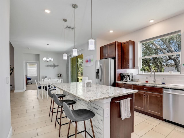 kitchen with a kitchen island, appliances with stainless steel finishes, a breakfast bar, decorative light fixtures, and sink