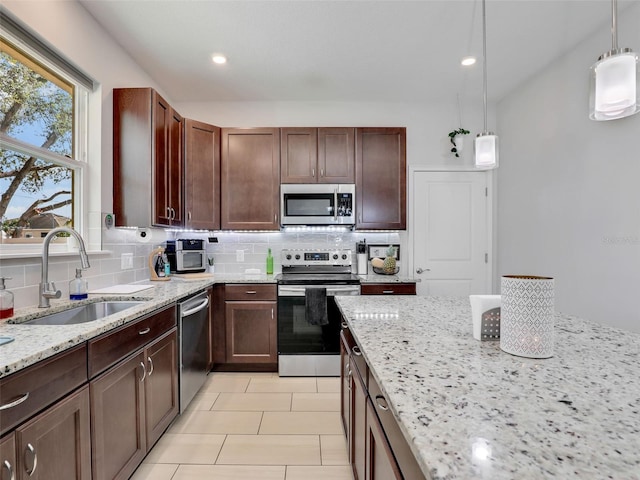 kitchen with sink, hanging light fixtures, appliances with stainless steel finishes, light stone countertops, and decorative backsplash