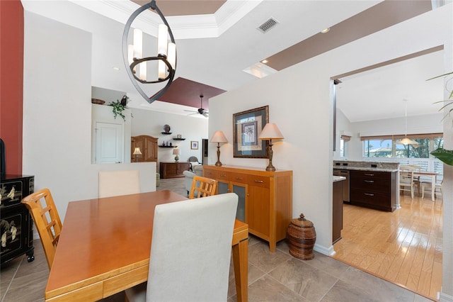 dining room featuring a tray ceiling, ceiling fan with notable chandelier, ornamental molding, and a wood stove