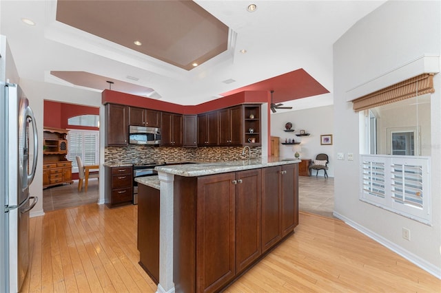 kitchen featuring an island with sink, appliances with stainless steel finishes, dark brown cabinetry, and a tray ceiling