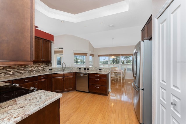 kitchen featuring pendant lighting, stainless steel appliances, a tray ceiling, and kitchen peninsula